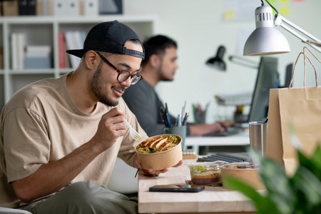 Young Asian man eating healthy meal while working, Businessman having a lunch break at the officeの写真素材