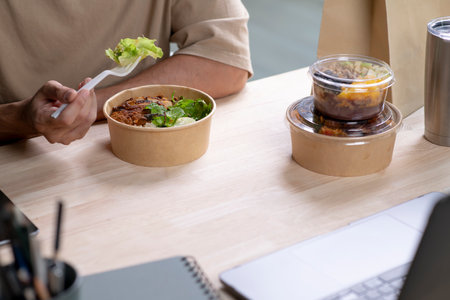 Young Asian man eating healthy meal while working, Businessman having a lunch break at the office, focus on foodの写真素材