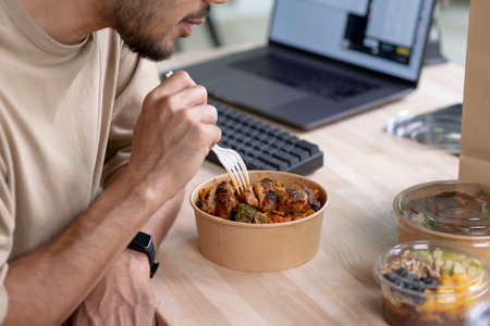 Young Asian man eating healthy meal while working, Businessman having a lunch break at the office