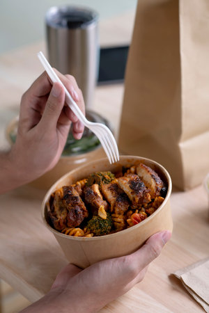 Close up hand holdjng paper bowl with healthy food, Young man, woman eating healthy meal while working, Businessperson having a lunch break at the office or homeの写真素材