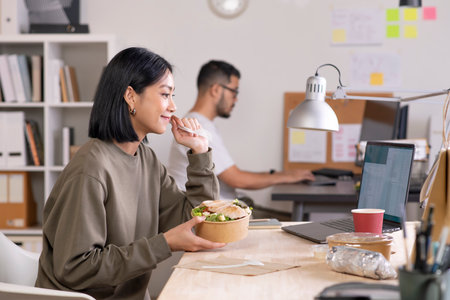 Asian woman eating healthy meal while working, Businesswoman having a lunch break at the officeの写真素材