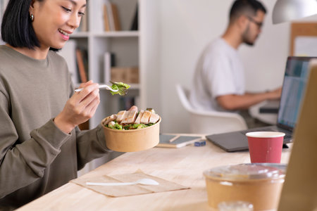 Asian woman eating healthy meal while working, Businesswoman having a lunch break at the officeの写真素材