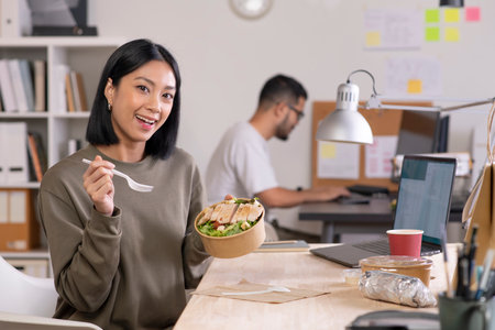 Asian woman eating healthy meal while working, Businesswoman having a lunch break at the officeの写真素材