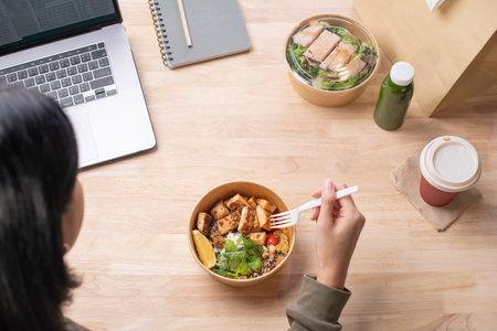 Asian woman eating healthy meal while working, Businesswoman having a lunch break at the officeの写真素材