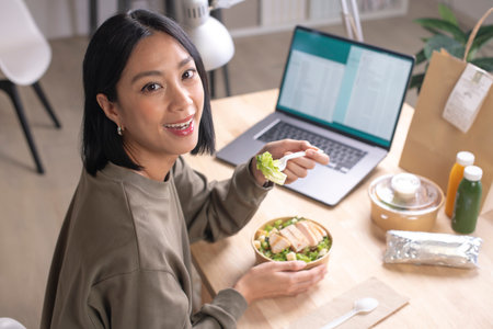 Asian woman eating healthy meal while working, Businesswoman having a lunch break at the officeの写真素材
