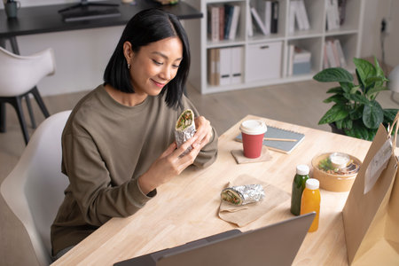 Asian woman eating healthy meal while working, Businesswoman having a lunch break at the officeの写真素材