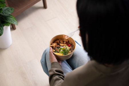 Asian woman holding and eating healthy meal at workplace, Businesswoman having a lunch break at home officeの写真素材