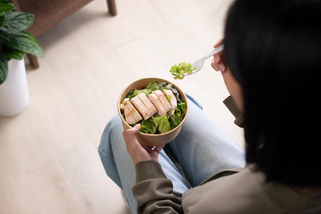 Asian woman holding and eating healthy meal at workplace, Businesswoman having a lunch break at home officeの写真素材