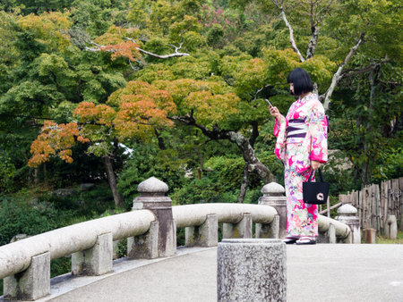 Kyoto, Japan - September 30, 2015: Young girl in colorful kimono checking her mobile phone - in Maruyama parkのeditorial素材