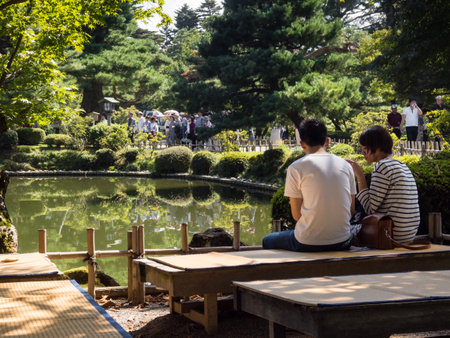 Kanazawa, Japan - September 28, 2015: Young couple sitting on a bench in Kenrokuen garden enjoying scenery on a sunny dayのeditorial素材