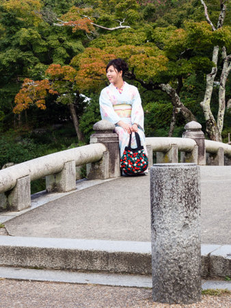 Kyoto, Japan - September 30, 2015: Young girl in beautiful kimono sitting on a stone bridge in...