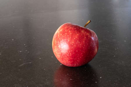 An apple a day, red tasty apple in dark background, kitchen table top, marble