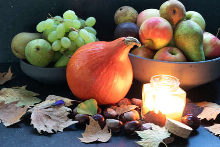 Organic orange pumpkin in a composition with grapes, peers, apples, autumn dried leaves, wine, candle light in a dark marble background. Harvest and cold timesの写真素材