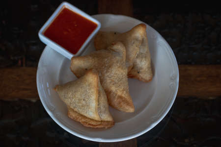 Samosas on a wooden table served with hot red sauce on white porcelain