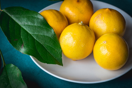 Persian Sweet lemons (Citrus limetta) on a white plate, green leaves and blue turquoise table
