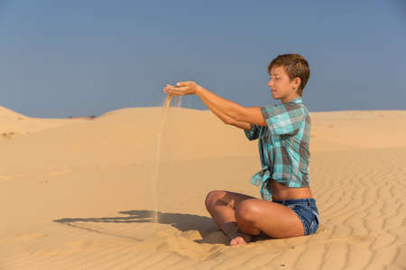beautiful young woman sitting on the beach in the sand dunes with sand in hands