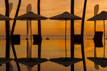 Sunset at a beach luxury resort in tropics.Summertime: beautiful cloudy dawn with parsols and palmsのeditorial素材