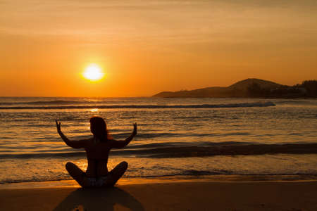 Woman practicing yoga on the ocean beach at sunset.の写真素材