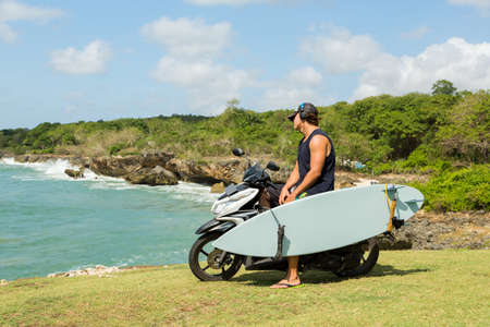 surfer man with surfboard and bike on the beachの写真素材