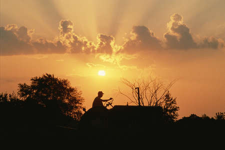 Silhouetted farmer on a tractor at sunsetのeditorial素材