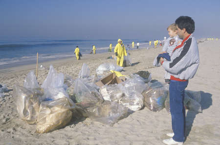A man holding his child observing efforts to clean up an oil spill in Huntington Beach, Californiaのeditorial素材