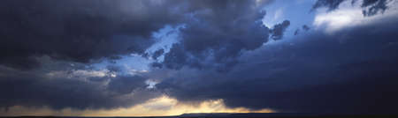 Dark clouds over the mountains of the Southwest. Sunlight on horizon starting to clear in western sky.の写真素材