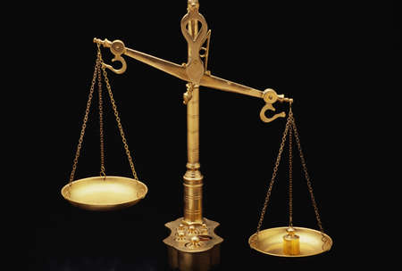 These are the golden Scales of Justice. They represent the legal system and courts. The scales here are shown unbalanced with the left side weighing heavier than the right. They are shown against a black background.のeditorial素材