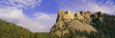 This is Mount Rushmore National Monument set into the mountain showing its natural surroundings against a blue sky. It shows the four faces of the Presidents George Washington, Thomas Jefferson, Theodore Roosevelt, and Abraham Lincoln.のeditorial素材