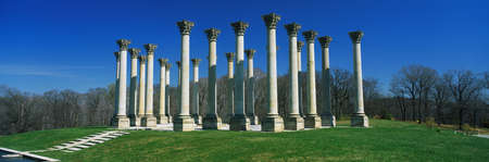 These are the historic National Capitol Columns at the National Arboretum. There is a stone walkway leading up to them surrounded by lawn against a blue sky.のeditorial素材