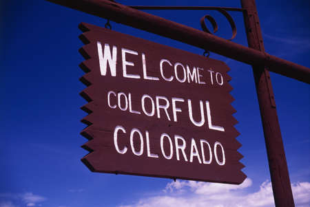 This is a road sign that says, Welcome to Colorful Colorado. It is a brown wood sign, painted with white letters against a blue sky. の写真素材