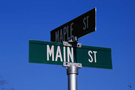 This is a street sign labeling the corner of Main Street & Maple Street. The sign is green with white lettering against a blue sky.の写真素材