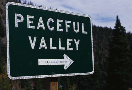 This is a road signs that says Peaceful Valley. There is white arrow pointing the way beneath the lettering.のeditorial素材