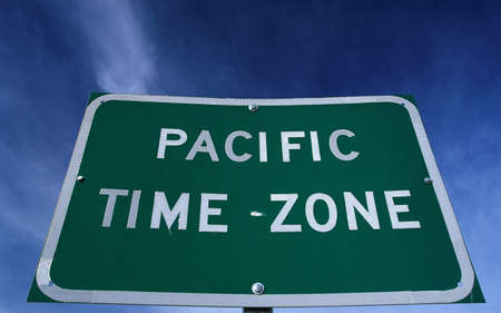 This is a road sign indicating a change to the Pacific Time Zone. The sign is green against a blue sky.の写真素材