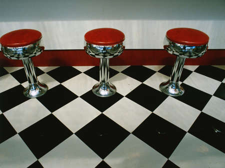 This is an art deco style restaurant. It has a black and white checkerboard tile floor with red vinyl stools next to the counter. It is a typical 50's style diner.の写真素材
