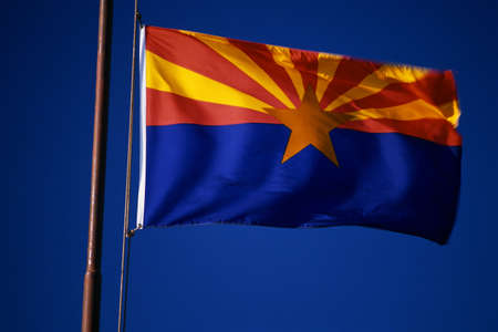 This is the Arizona State Flag waving in the wind. It is situated on a flagpole against a blue sky. At the center of the flag is a star.の写真素材