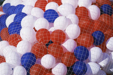 Red, white, and blue balloons being held by netの写真素材