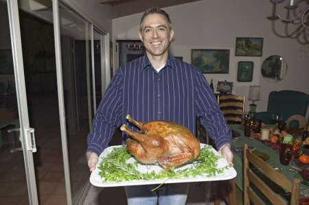 Man holds cooked turkey in front of a table set for Thanksgiving dinner in Ojai, Californiaのeditorial素材