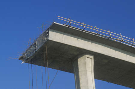 A concrete freeway structure ends abruptly with iron support structures sticking out and safety...