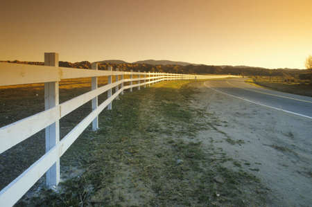 A white fence follows the path of Route 33 near Ojai into the sunsetのeditorial素材