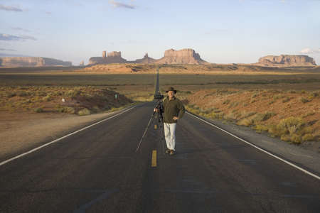 Professional photographer with camera on tripod standing in middle of Route 163, Monument Valley, Southern Utahのeditorial素材