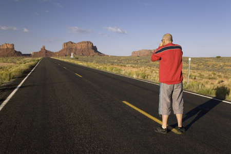 Tourist with red shirt taking picture from middle of road, on Route 163 to Monument Valley in Utah near Arizona border, Navaho Nationのeditorial素材