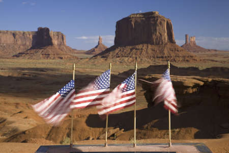 US Flags blowing in wind in front of red buttes and colorful spires of Monument Valley Navajo Tribal Park, Southern Utah near Arizona borderのeditorial素材