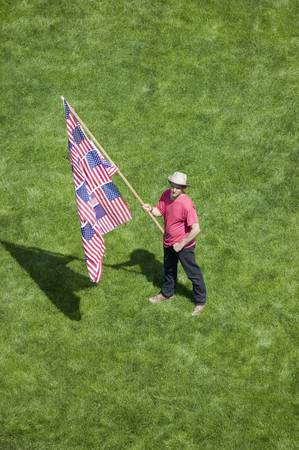 A patriotic man with a US Flag made of many US Flags stands alone in a green grass lawn at an anti-Iraq War protest march in Santa Barbara, California on March 17, 2007のeditorial素材
