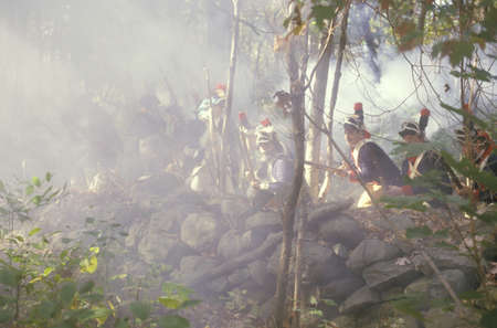 Men dressed in 18th century American military costume fire muskets and charge through mist during a...