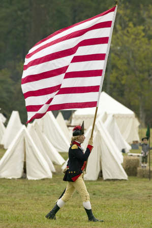 An early American flag is flown by solider on his way to Surrender Field at the 225th Anniversary of the Victory at Yorktown, a reenactment of the siege of Yorktown, where General George Washington commanded 17,600 American troops and French Comte de Rochのeditorial素材