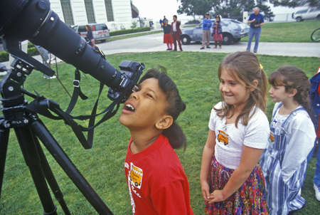 African American school girl looking through telescope at Solar Eclipse with friends waiting in line, Griffith Observatory, Los Angeles, CAのeditorial素材