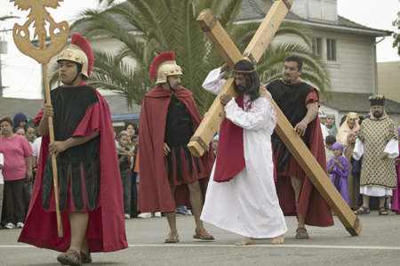 An actor portraying Jesus Christ carrying a cross past crowds on Good Friday, Easter, during the Passion play, a dramatic reenactment of the trial, torture and death of Jesus Christ at Christ the King Church and Our Lady of Guadalupe Parish, Oxnard, Califのeditorial素材