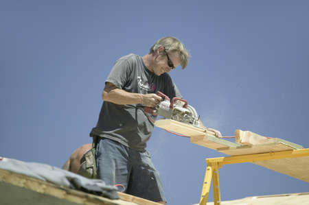Carpenter sawing board on roof on new house construction, Ojai, California