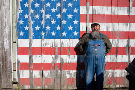 Augusta, Maine - June 10, 2012 - An elderly man standing in front of a painted US flag on his shed のeditorial素材
