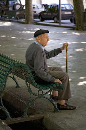 Older man with cane sitting on bench in market area of La Seu d'Urgell, (Sa Seu d'Urgell) in Catalunya, Spainのeditorial素材